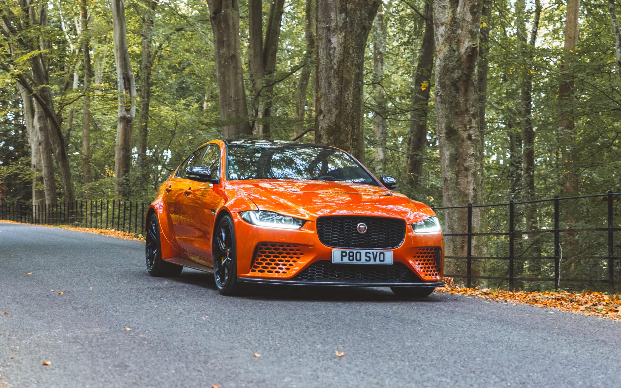 An orange Jaguar Project 8 driving through autumn woodland.
