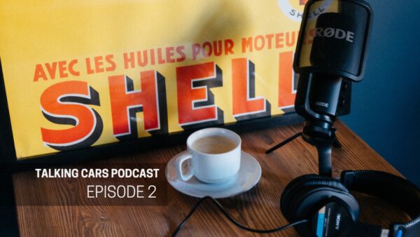 A coffee and podcast microphone on a table with a vintage motoring poster.