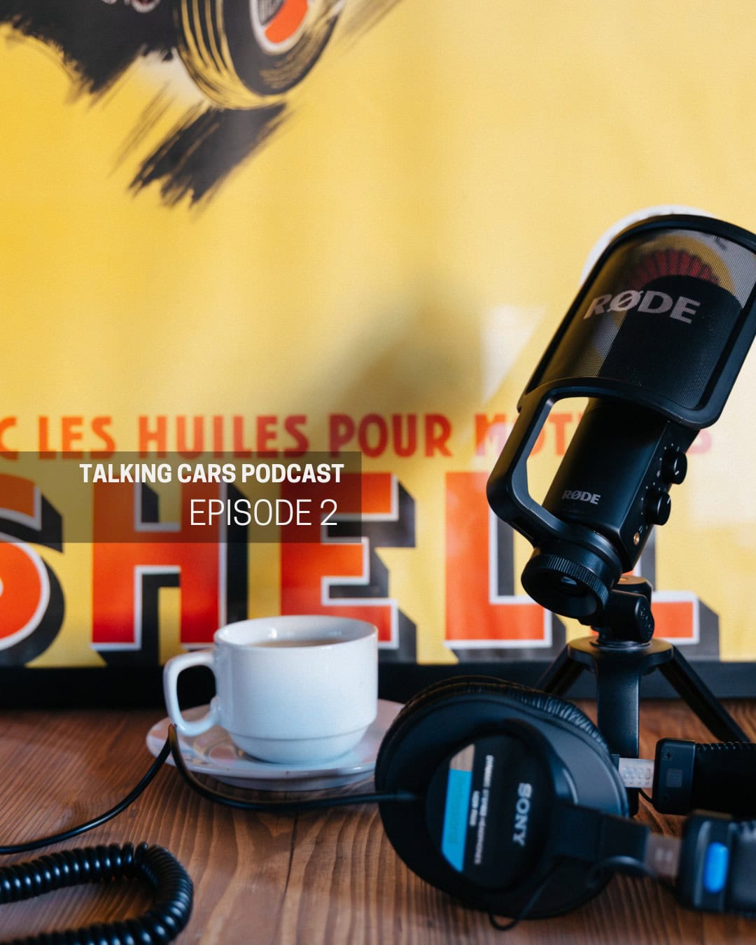A coffee and podcast microphone on a table with a vintage motoring poster.