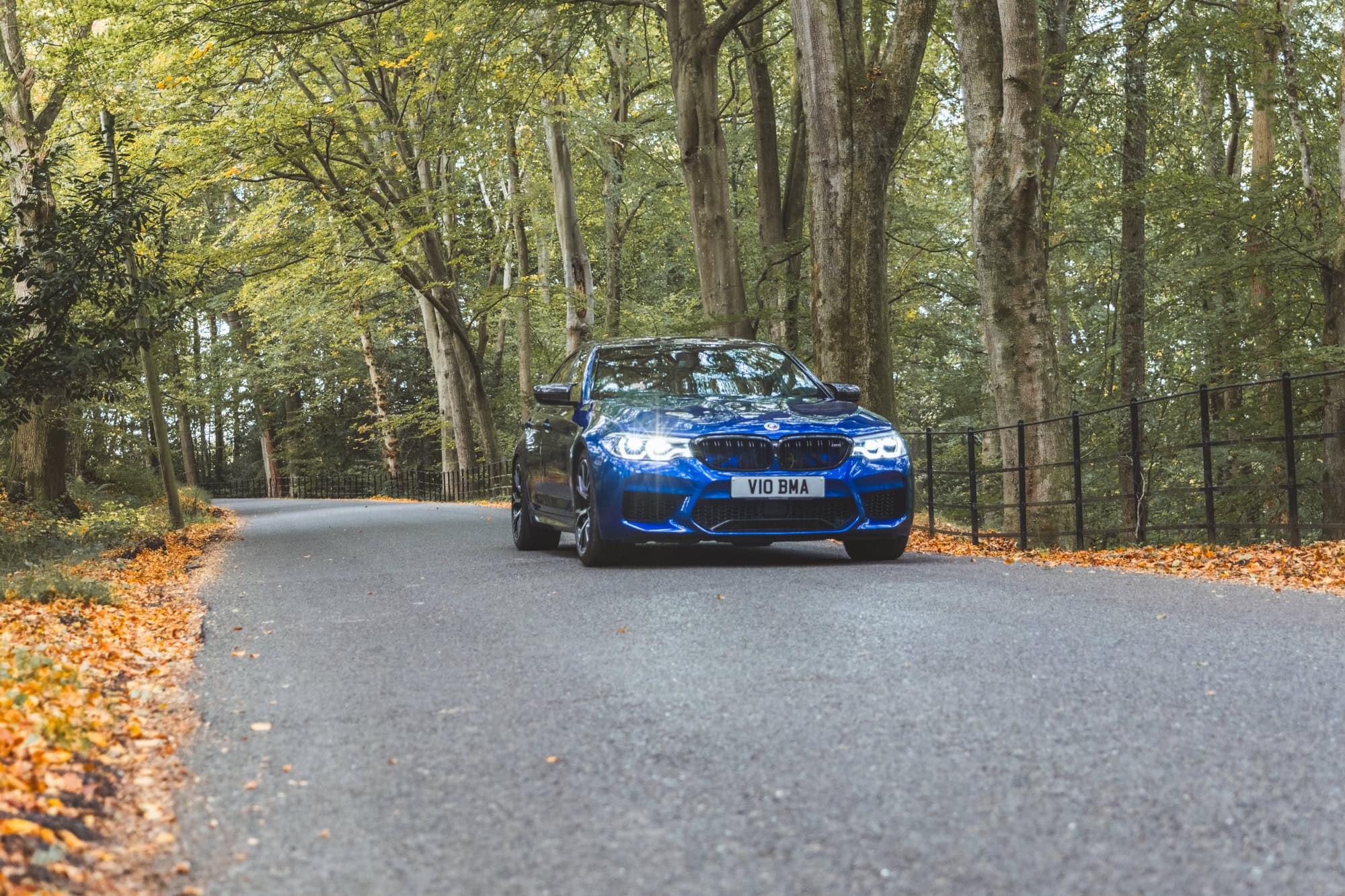 A Marina Blue F90 BMW M5 Competition driving down a forest road.