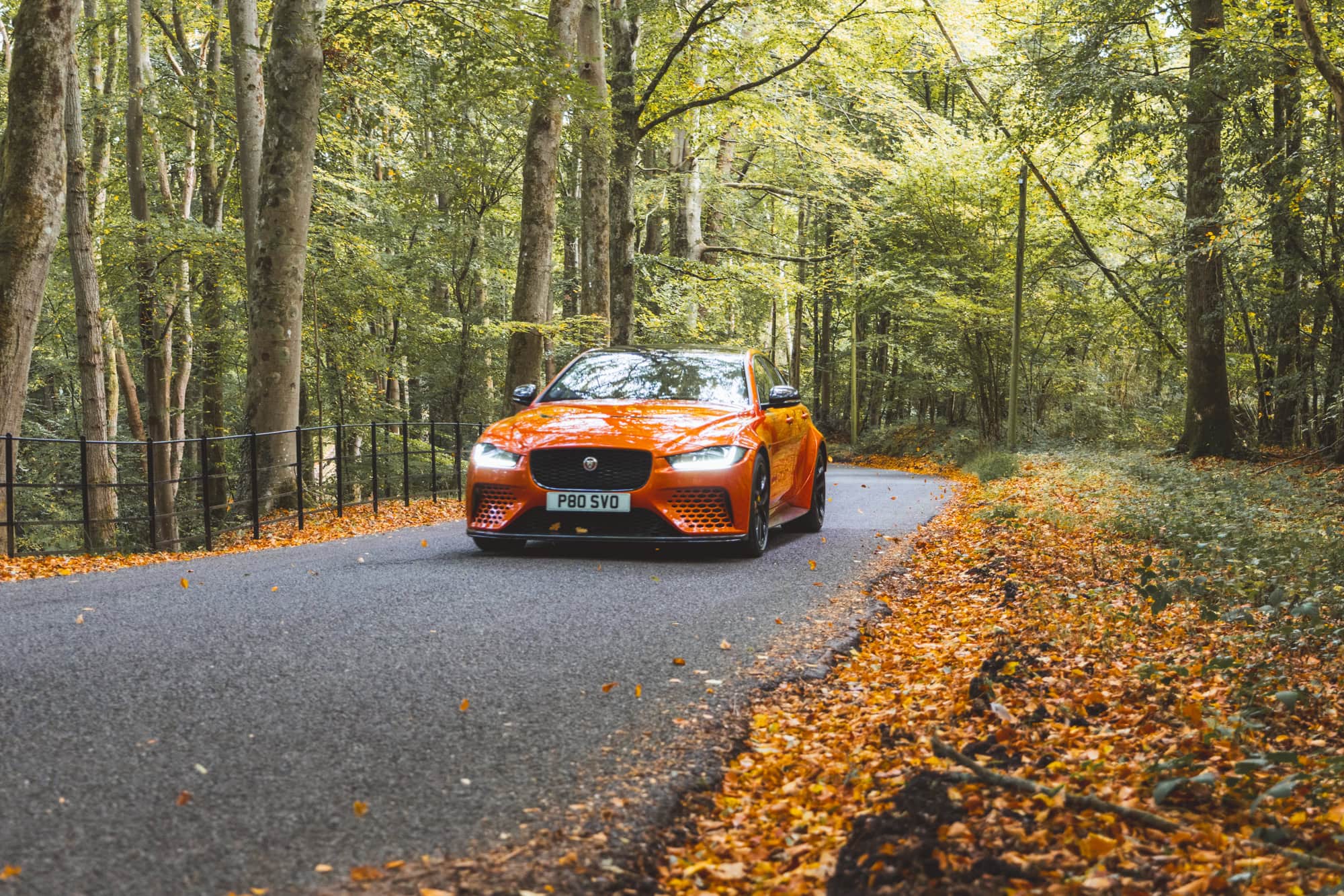 An orange Jaguar Project 8 saloon driving down a forest road.
