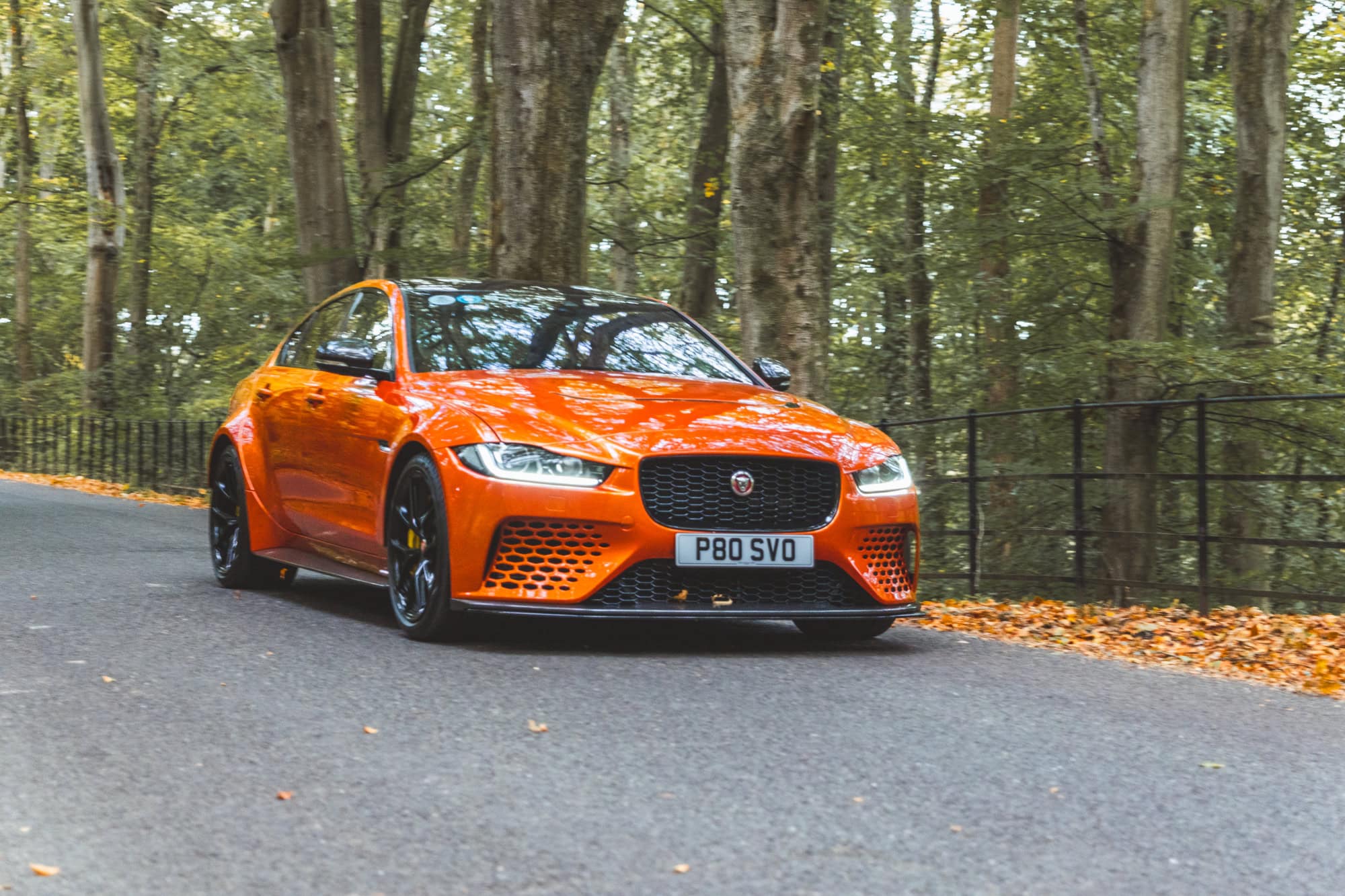 A Valencia Orange Jaguar Project 8 saloon driving down a forest road.