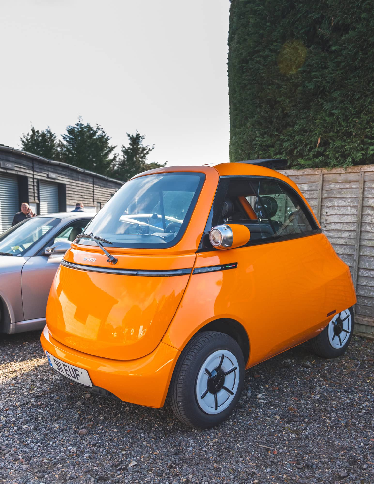Hero motor company open day showing an orange microlino in front of trees and fence panel