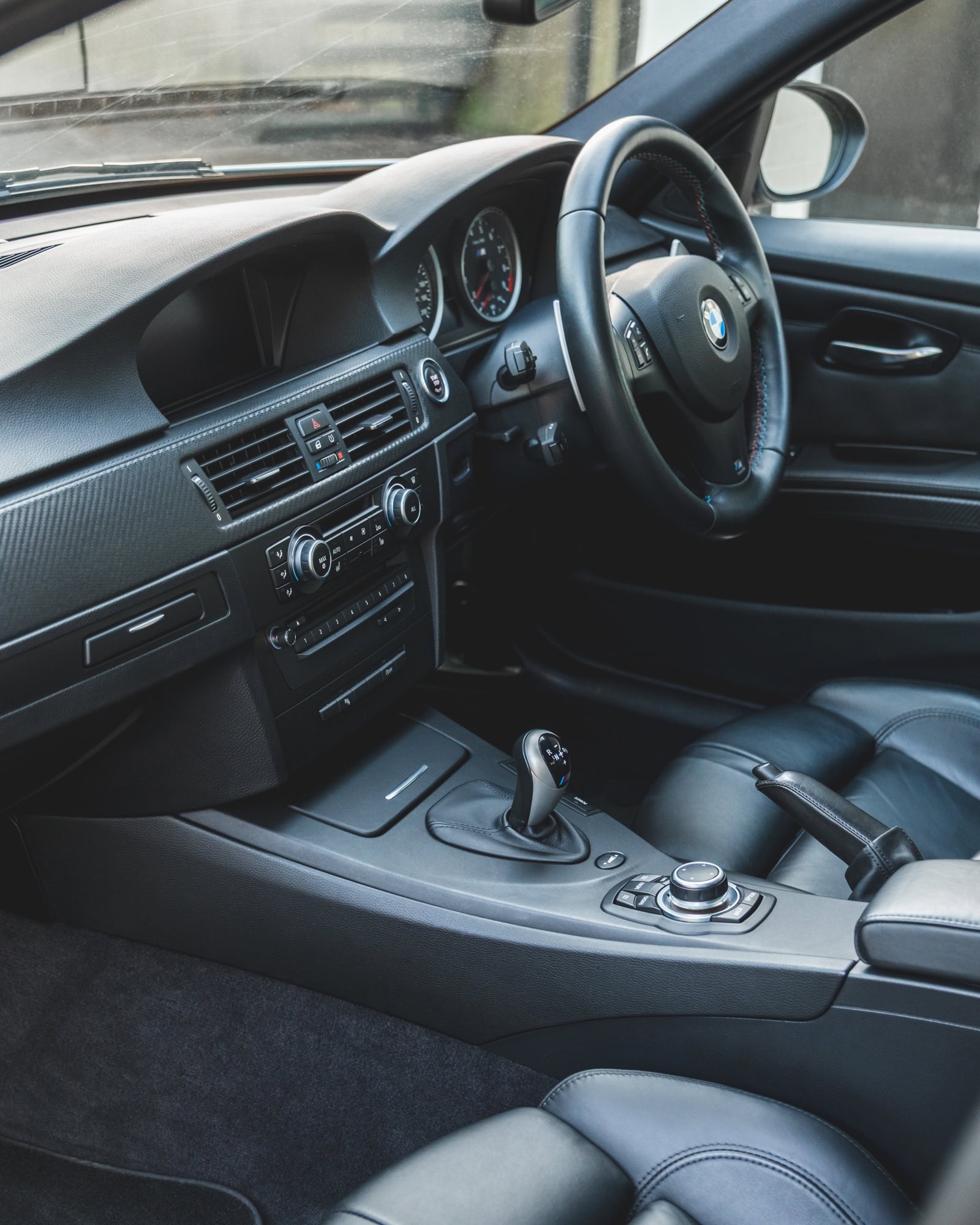 Nearside view into the interior of BMW E90 M3 showing steering wheel centre console DCT gearbox and black leather seats