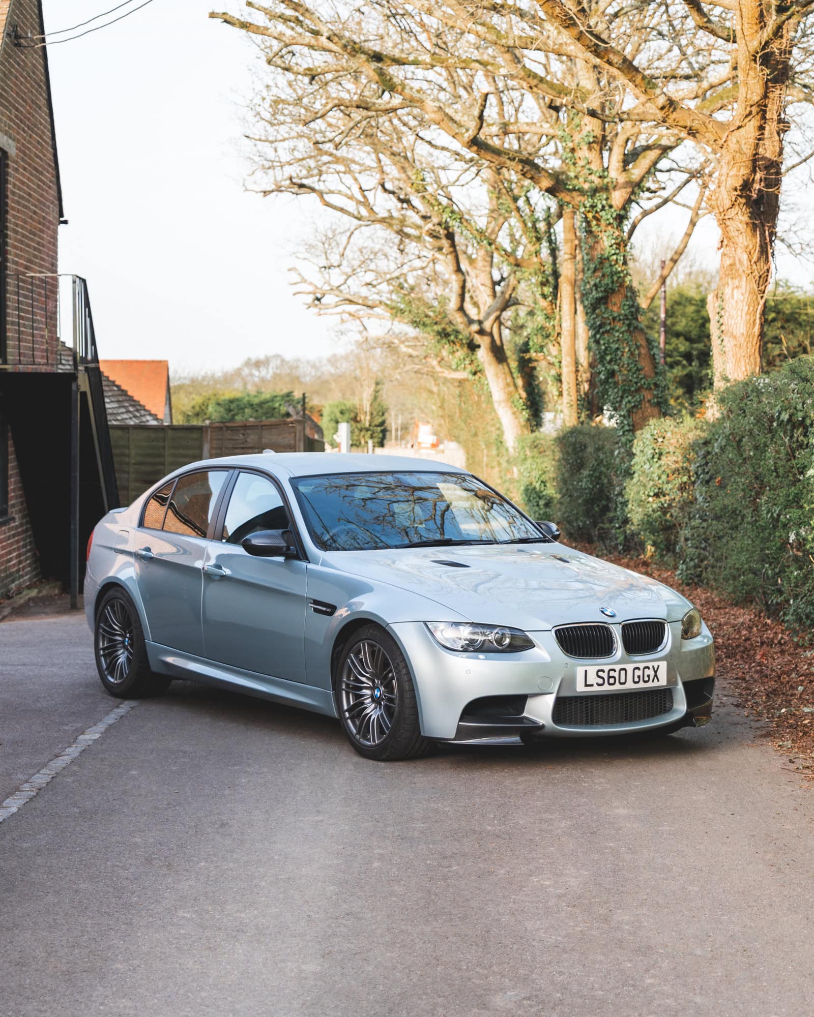 Front offside view of BMW E90 M3 Silverstone II showing alloy wheels parked on a lane with trees and fencing in the background