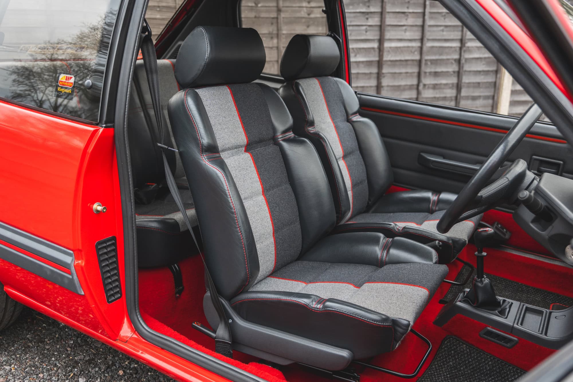 Offside view into interior of Peugeot 205 GTI showing partial leather seats steering wheel and red carpet