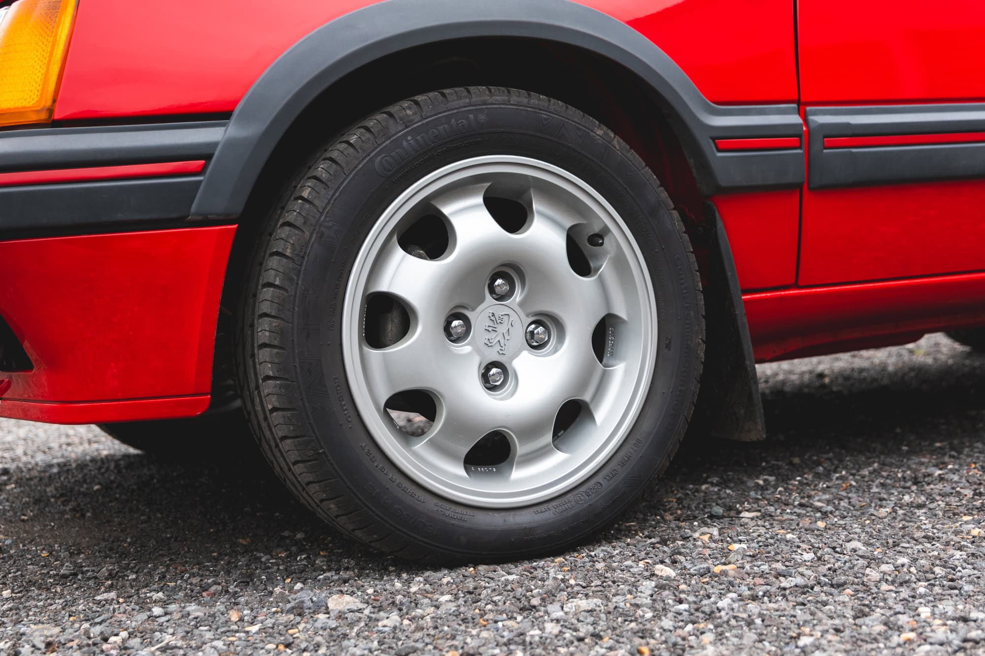 Close up view of alloy wheel on cherry red Peugeot 205 GTI showing lower body panels