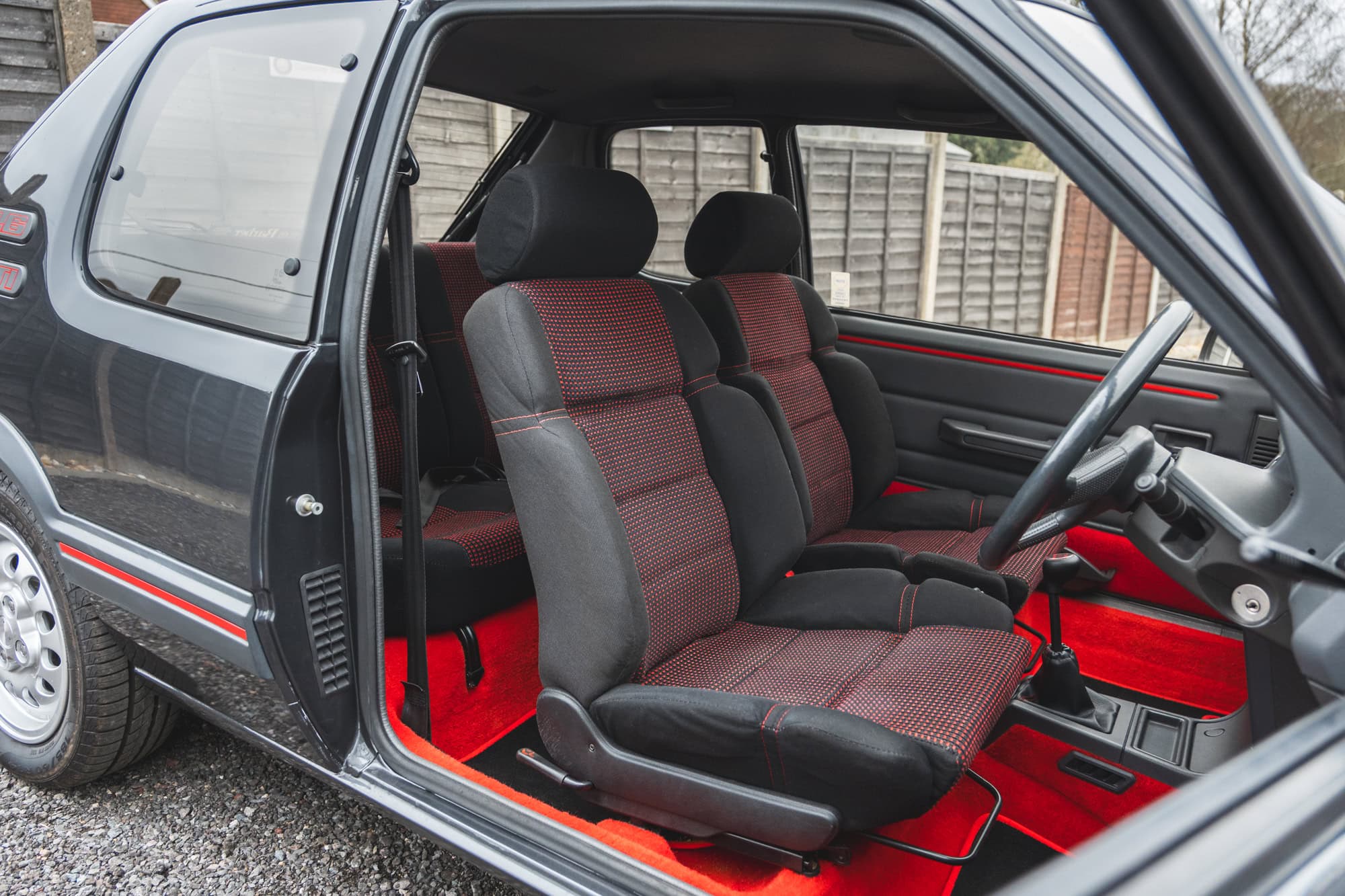 Landscape picture of offside view into interior of Peugeot 205 GTI showing front seats and red carpet