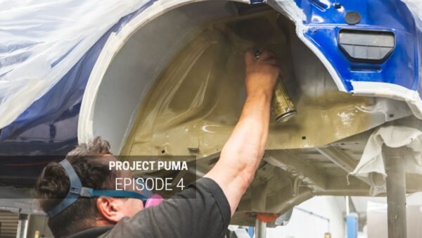 A mechanic holds a spray can up to the arch of a ford racing puma.