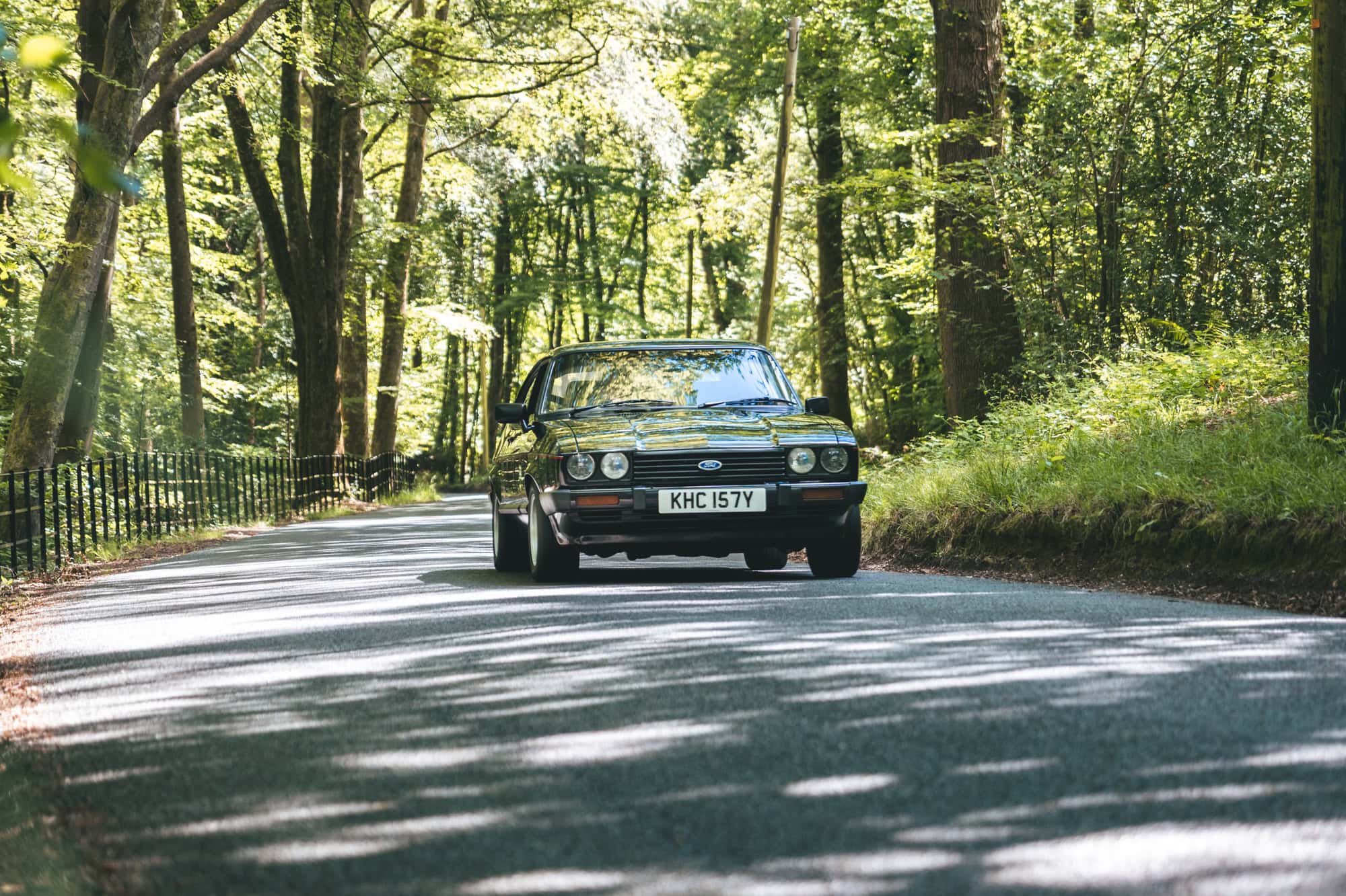A black MK3 Ford Capri on a forest road.