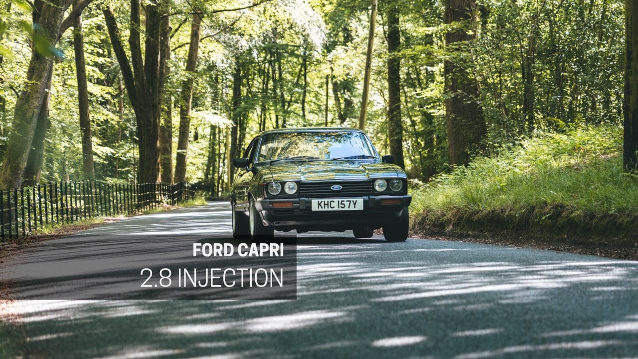 A black MK3 Ford Capri 2.8 Injection drives through a forest road.
