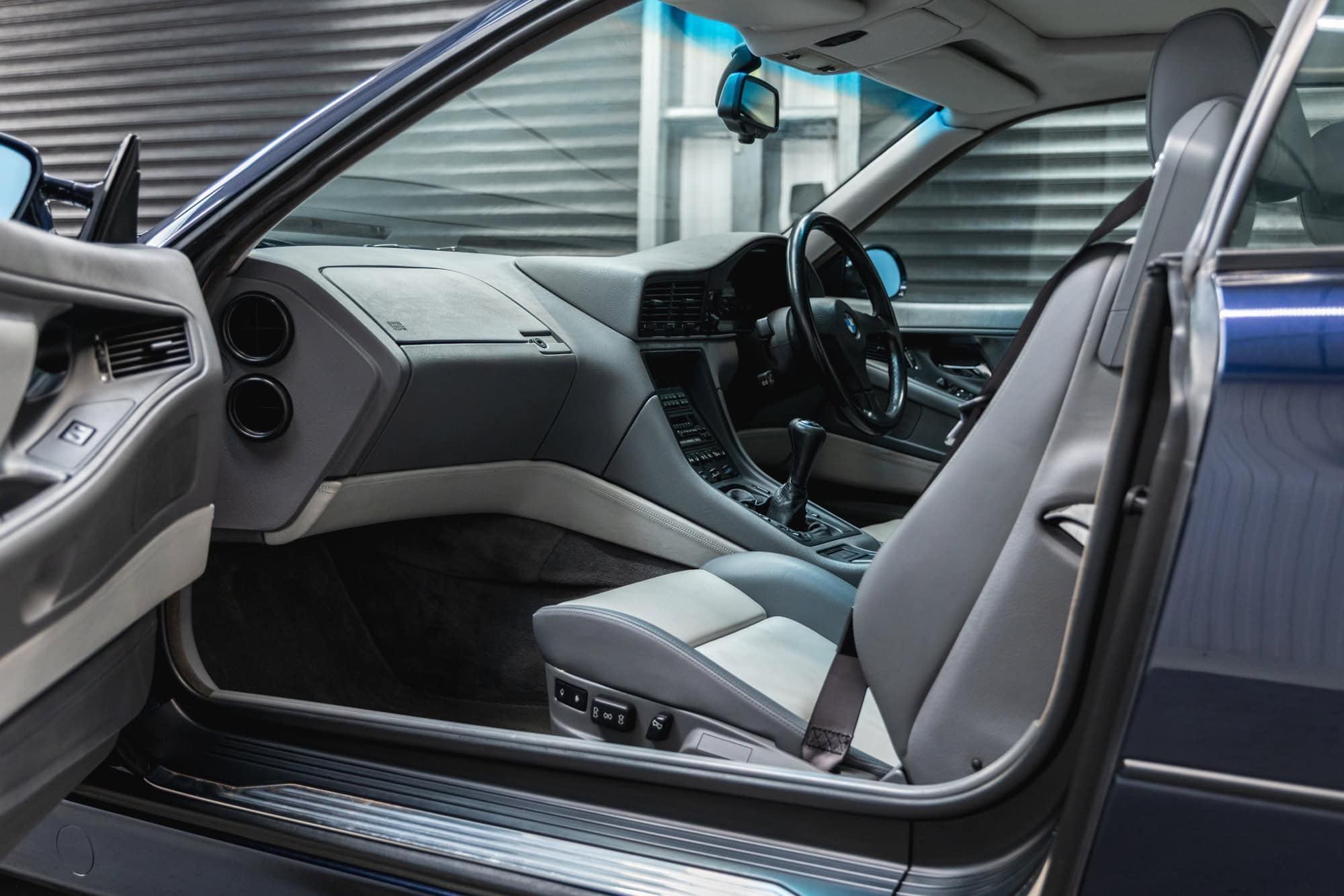 Interior and passenger side dashboard of a BMW 850 CSI coupe in orient blue metallic with silver and grey leather interior.
